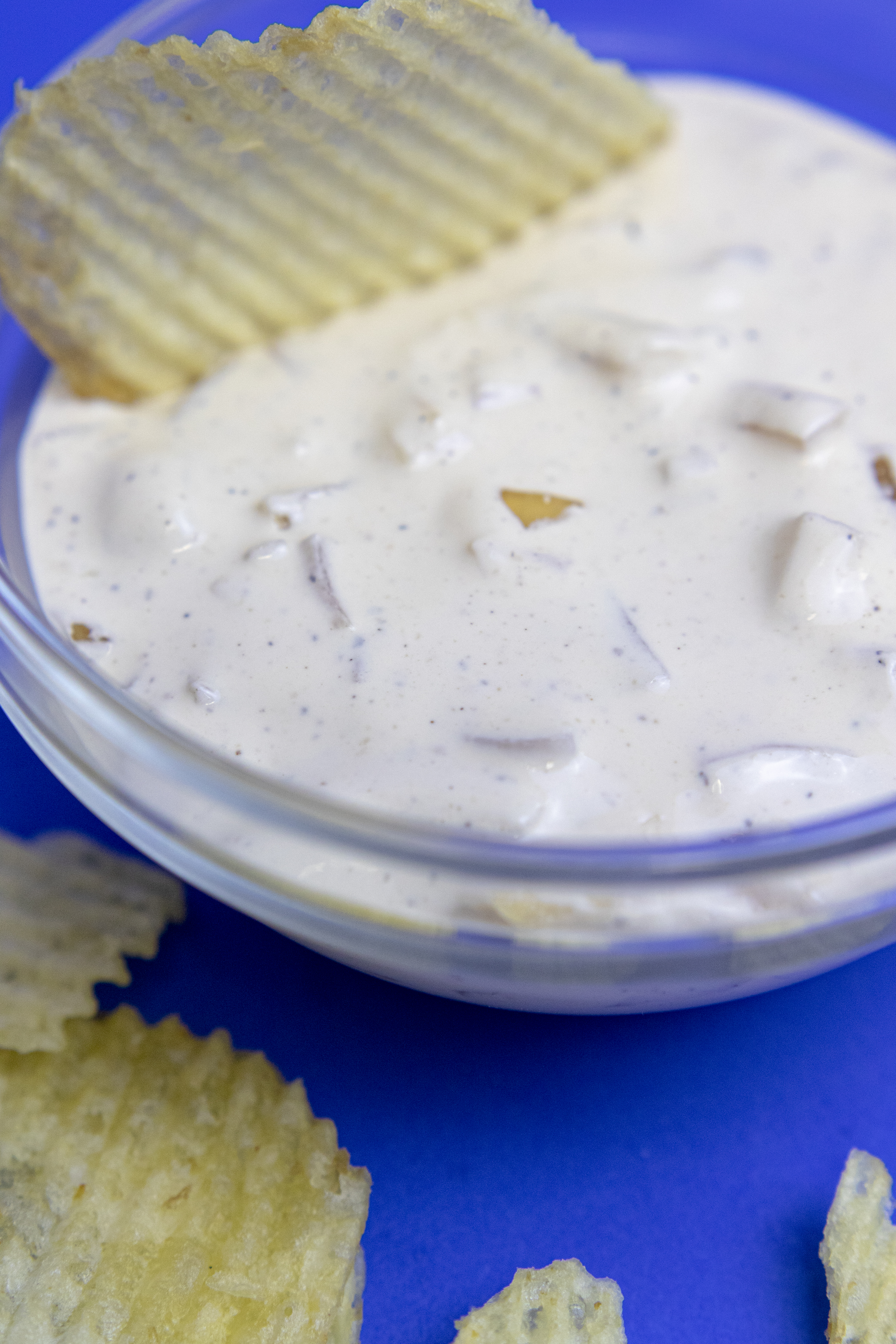 ribbed potato chip in a clear bowl of homemade onion dip on a blue backdrop