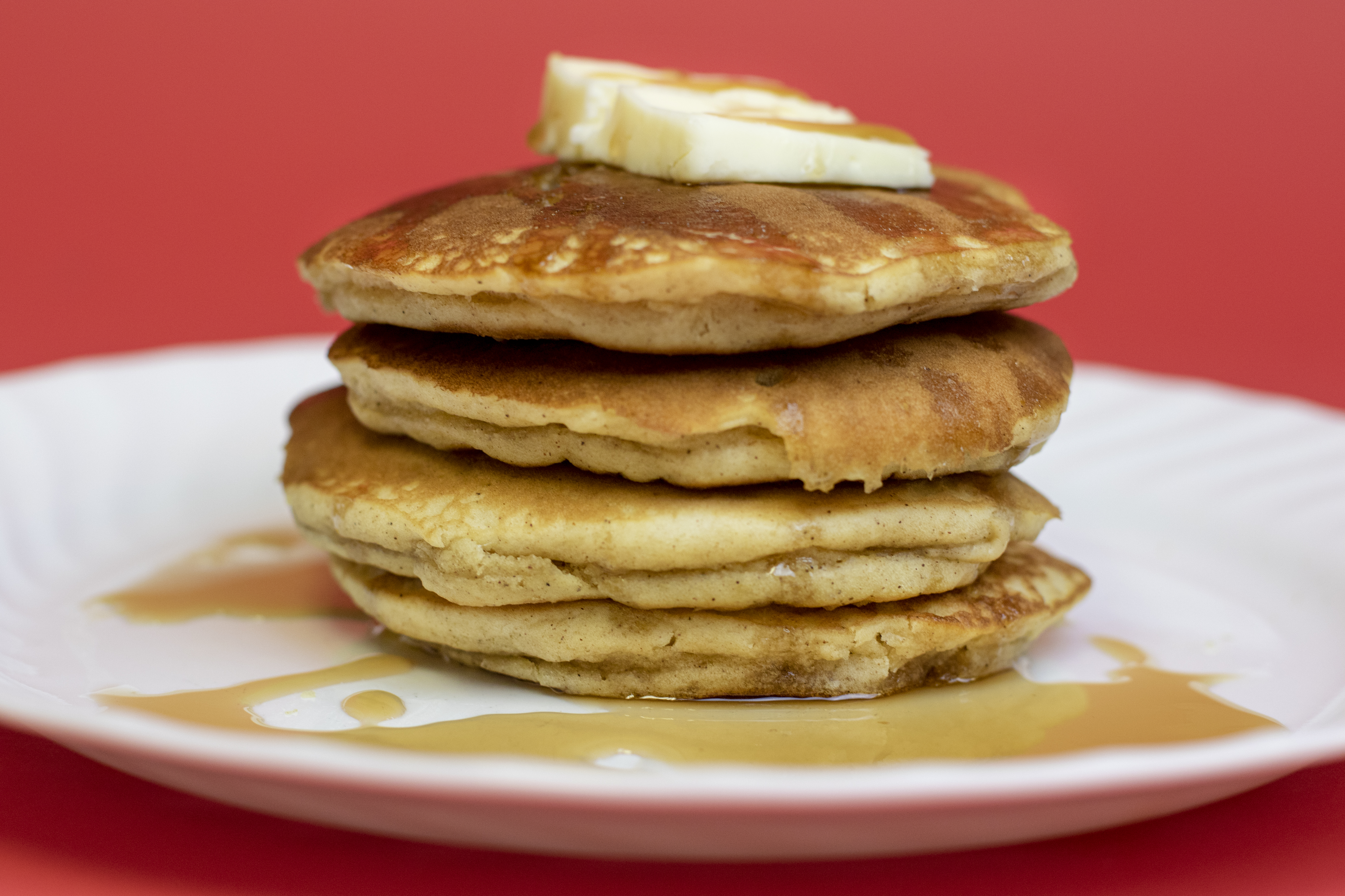 Apple cinnamon pancakes with butter and syrup drizzling over the sides on a white plate with a red backdrop