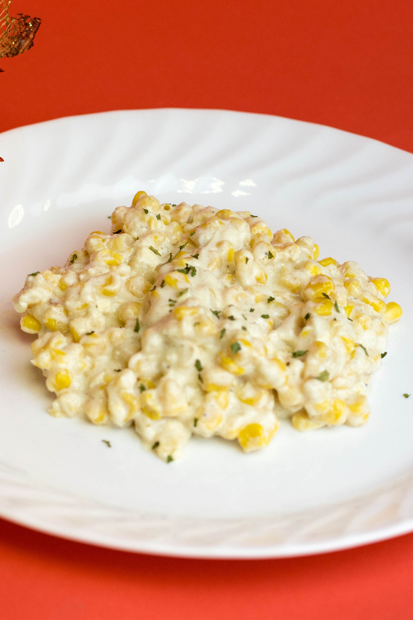Creamed corn on a white plate laying on a flat red background.