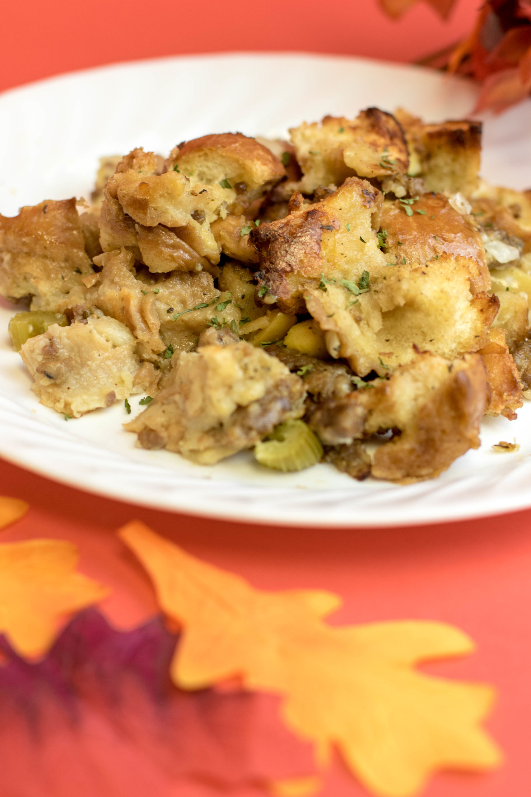 Thanksgiving stuffing on a white plate surrounded by fall leaves sitting on a red background.