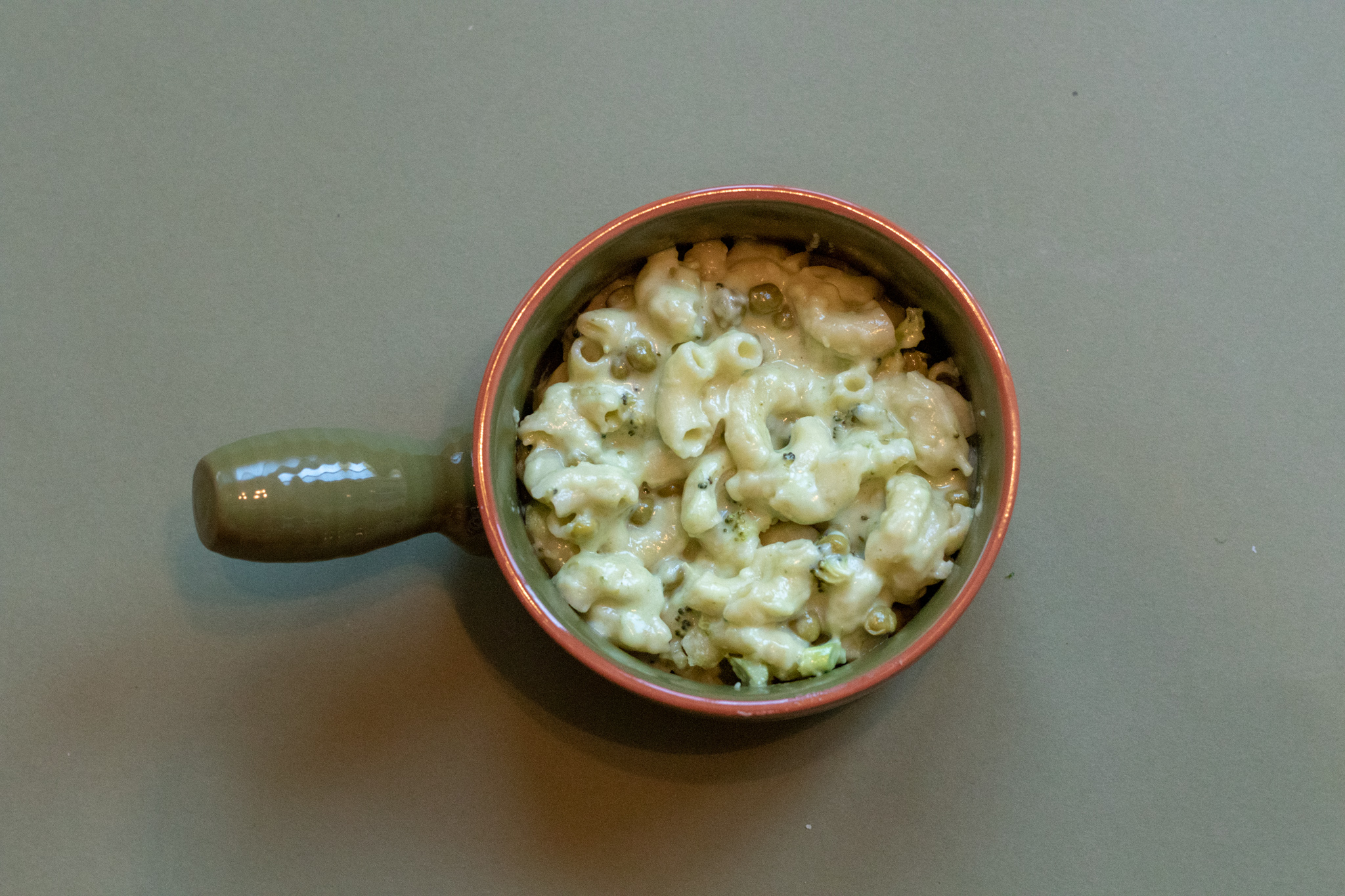 Veggie Macaroni and cheese in a green bow with an orange rim on a green background.